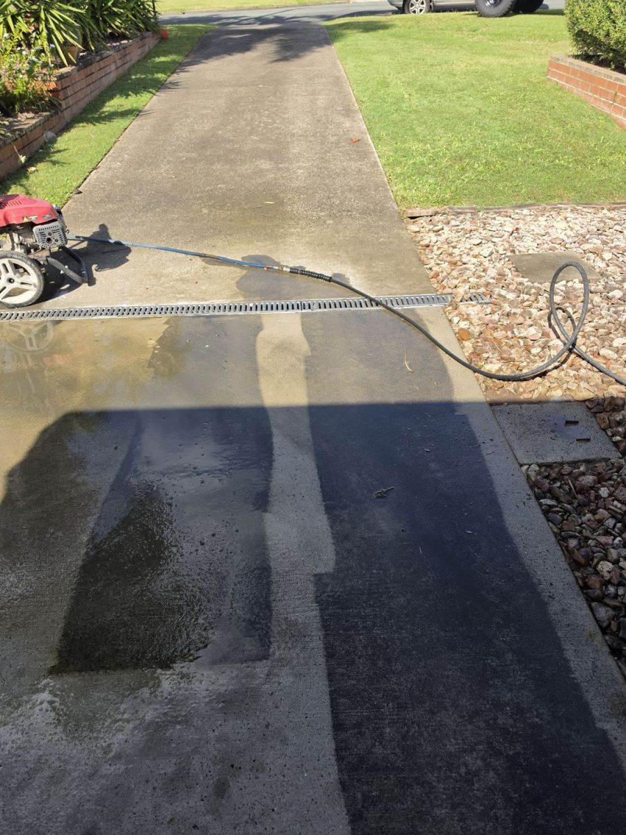 Driveway part way through pressure washing, clean strip beside dirty concrete
