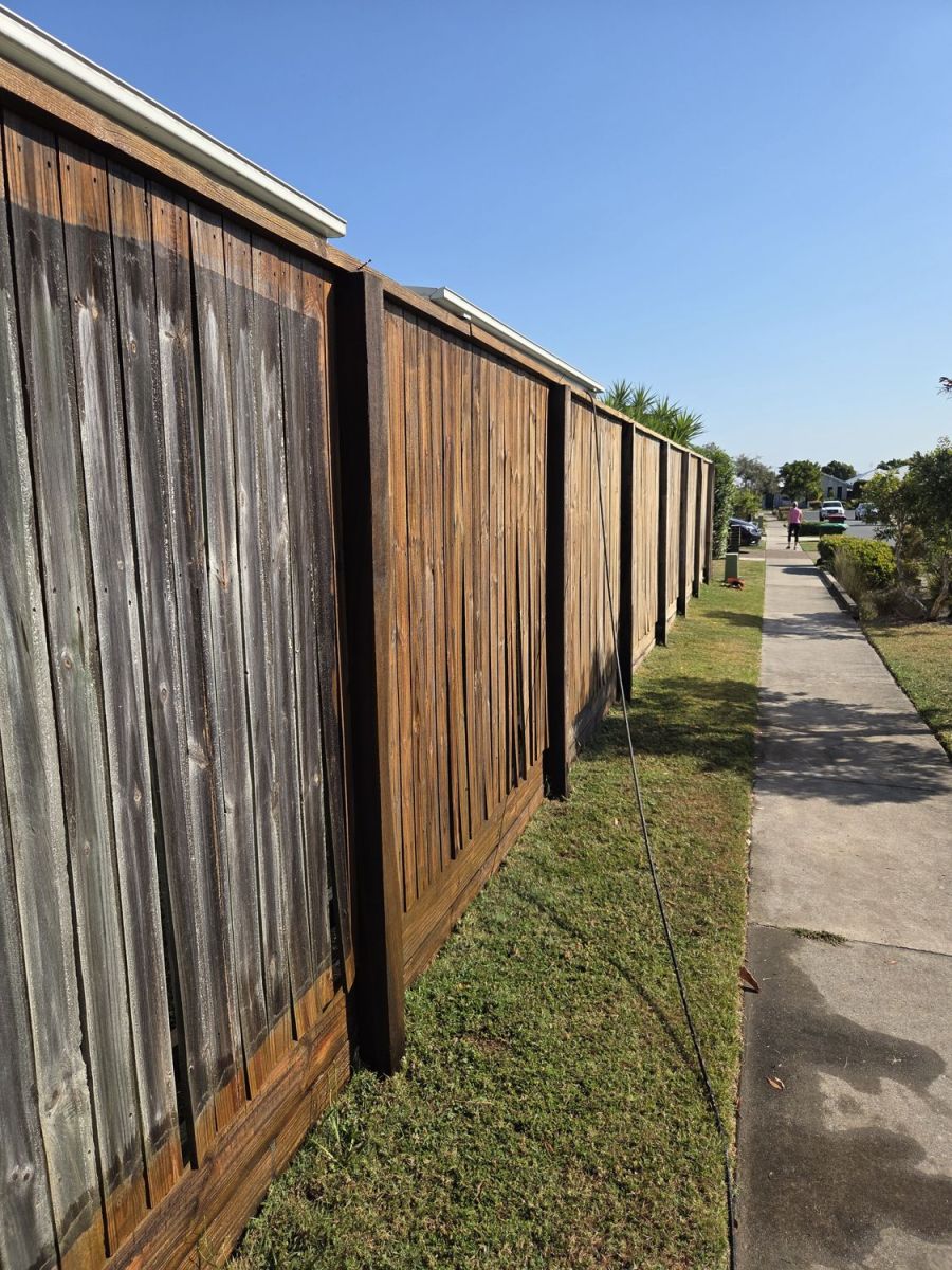 Timber fence part way through washing, grey panels beside cleaned panels