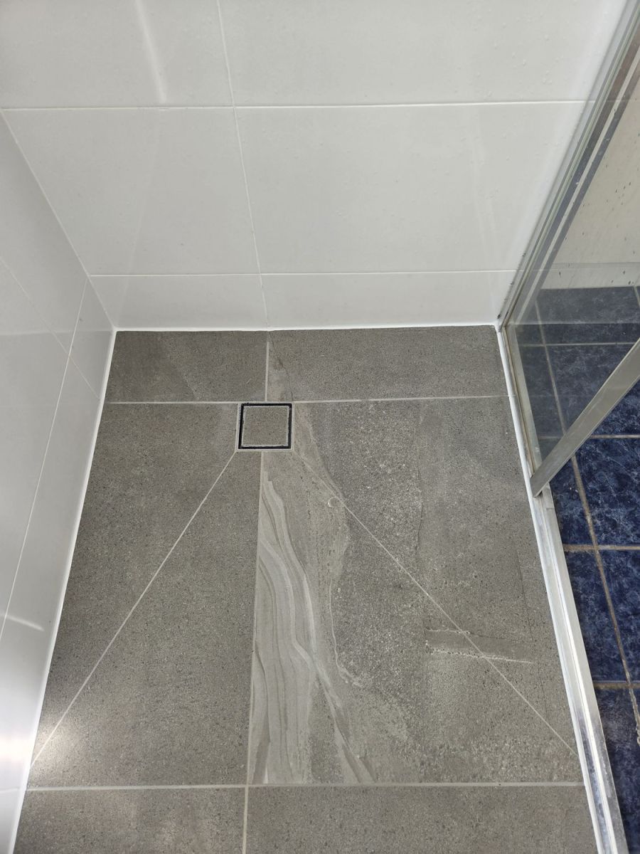 Shower floor with new grey tiles and a square drain